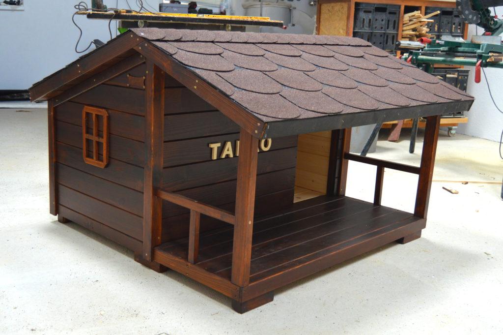 Psia búda CASSIDY s áčkovou strechou, krytou pevnou terasou s okrasným zábradlím, ozdobnými postrannými okienkami, v odtieni orech, s hnedou krytinou a menovkou TADAO #1